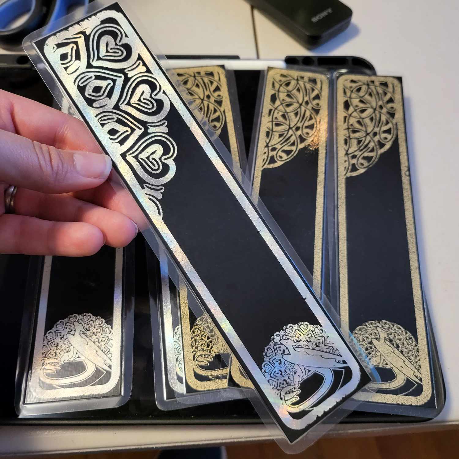 Stacks of laminated bookmarks on black card with gold foiled designs of dragons.