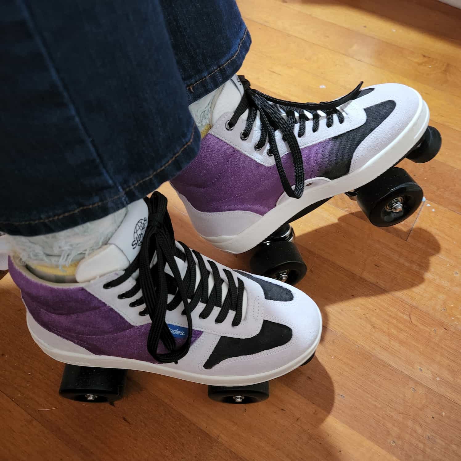 Sneaker rollerskates (slades) with black wheels, black toe stops and black laces. The skates are light grey, with panels painted in purple and black.