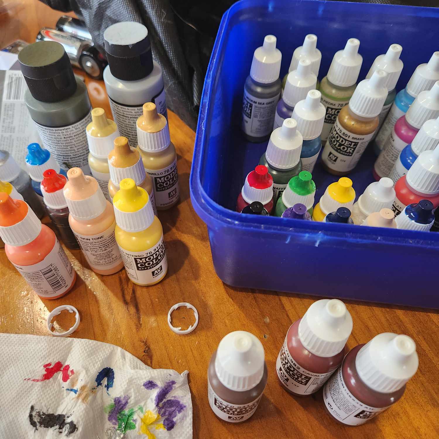 Model paints in a range of colours on a wooden surface and stored in an empty ice cream container. A paint rag shows some of the paint in the bottom left corner.