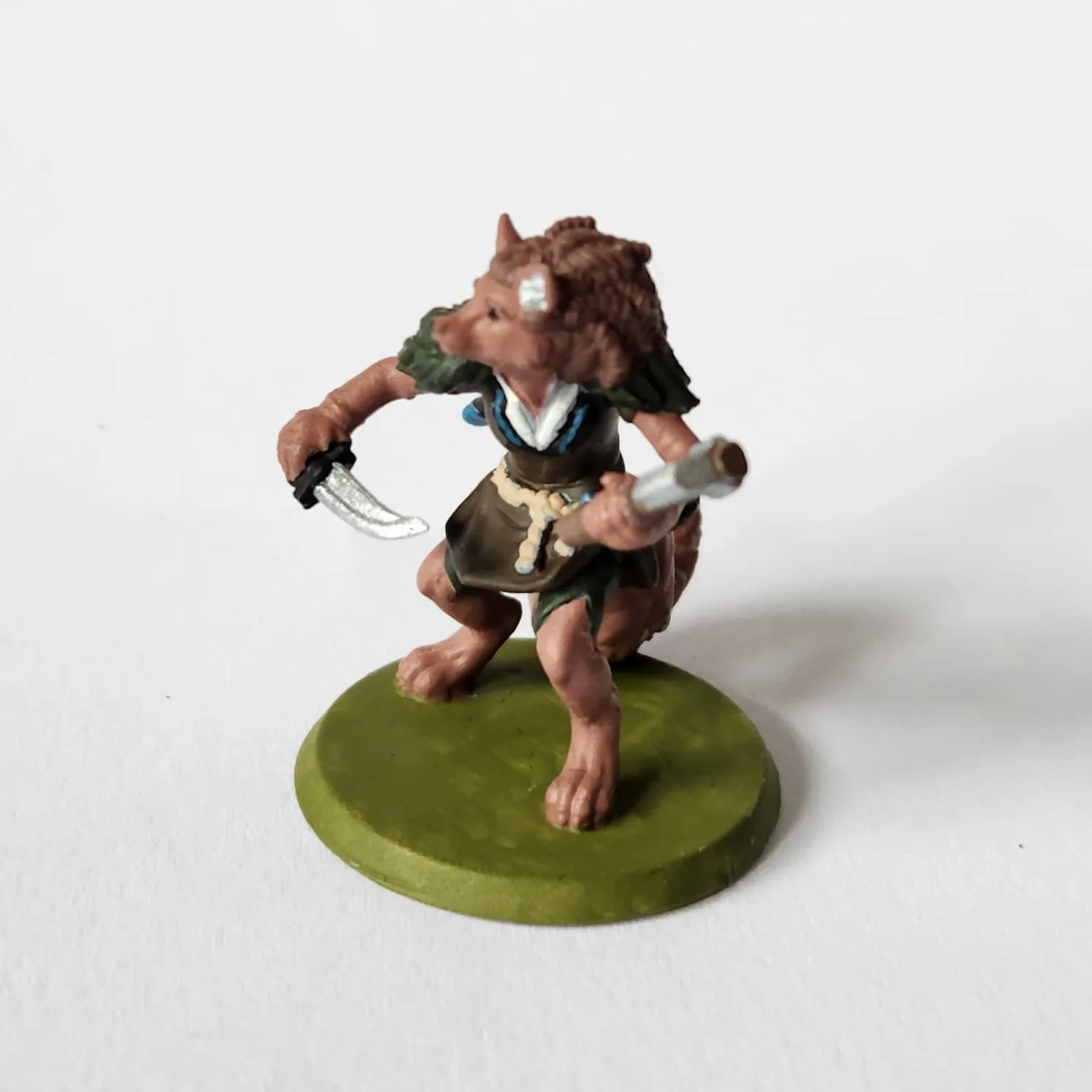 Miniature of a female fox-like humanoid. She has a long snout, large ears, braided hair. She is posed defensively with a dagger held in one paw, and a scroll in the other. She has on a long green tunic with white shirt underneath, and green shorts. Her feet are bare.