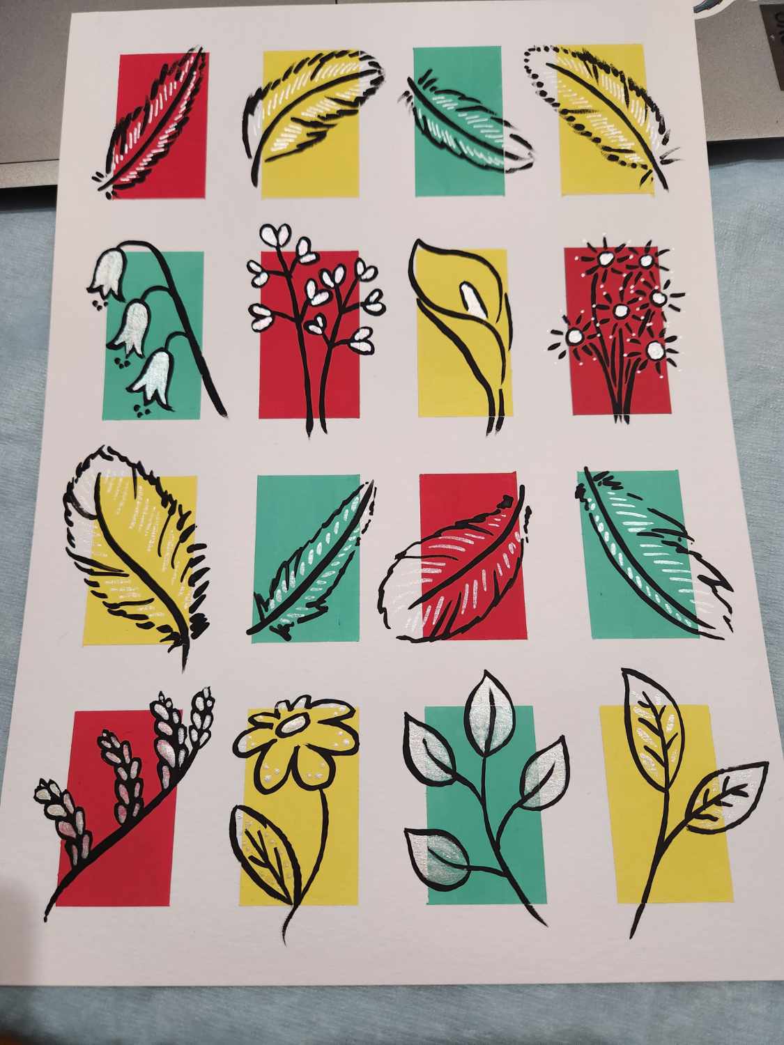 A4 white paper with a 4x4 grid of rectangles in red, yellow and turquoise. Each rectangle has either a simple flower or feather design drawn over it, overlapping the edges of the rectangle, in black ink with white ink highlights. Top and third rows are feathers, second and fourth rows are flowers.