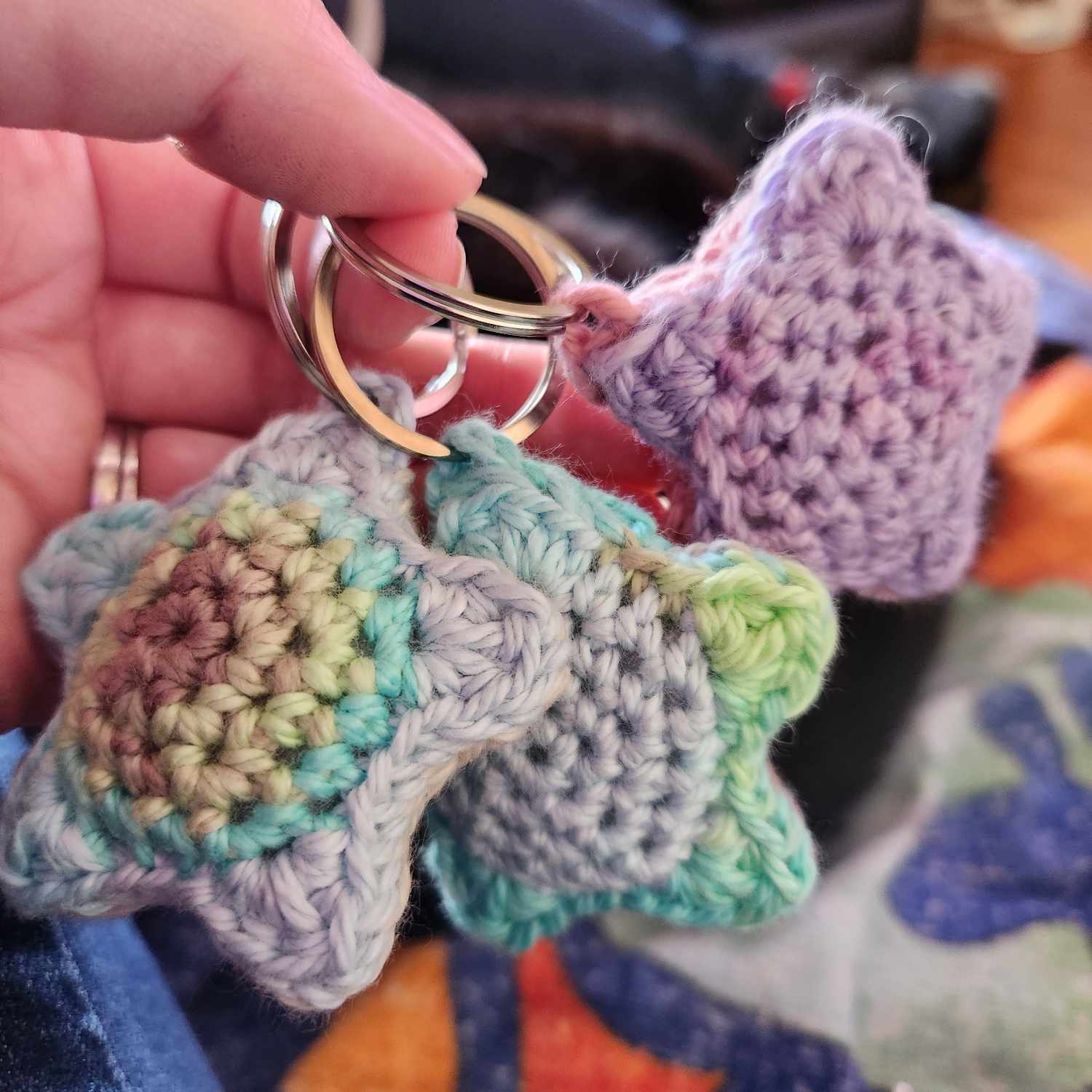 Three colourful and puffy crochet stars on keyrings hend in a hand.