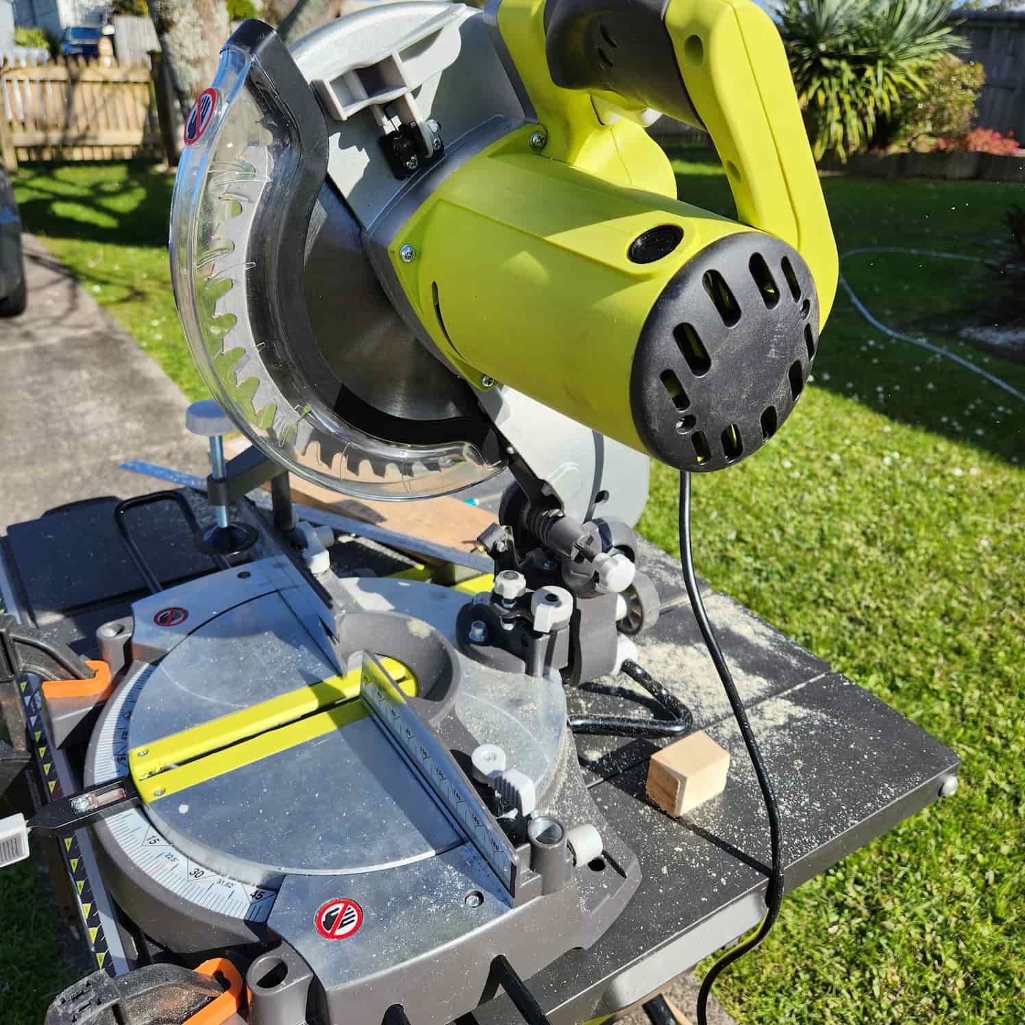 Yellow circular saw set up outdoors. There is sawdust and a piece of offcut wood.