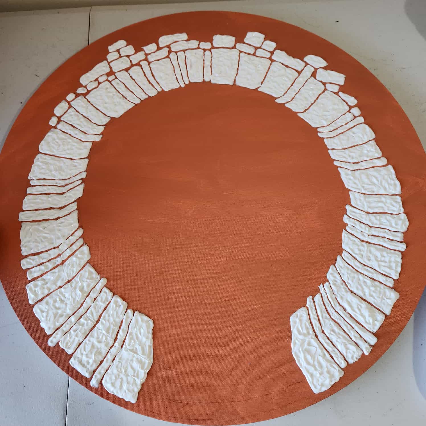 Round stretched canvas painted orange. The modelling paste is done, showing a round stone arch design.