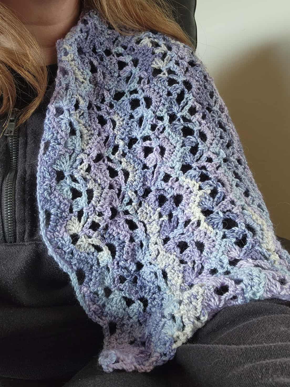 A purple, light blue and off-white woolen shawl in a lace design draped over a shoulder.