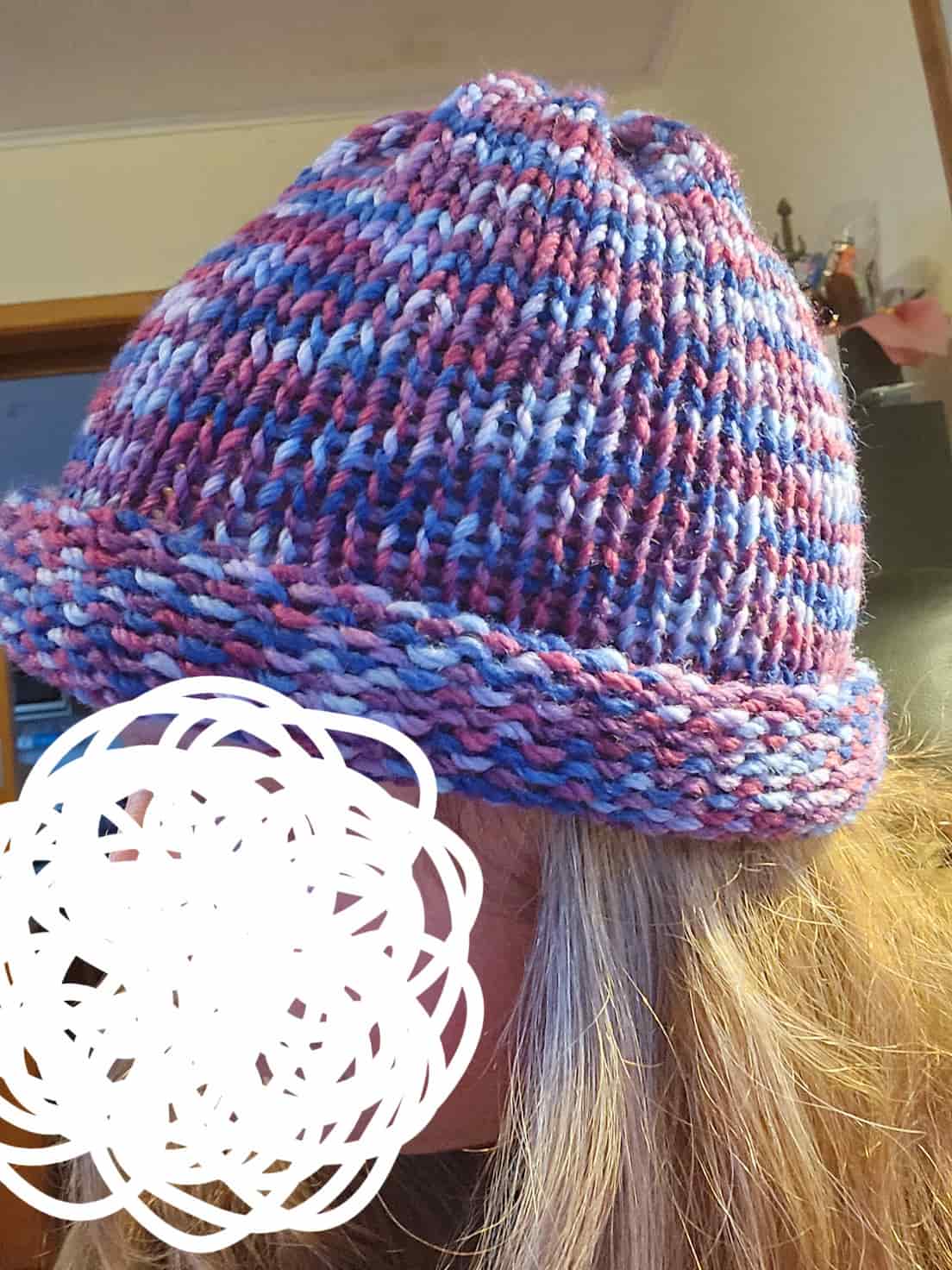 A beanie with wool that has light blue, dark blue, pink and purple.