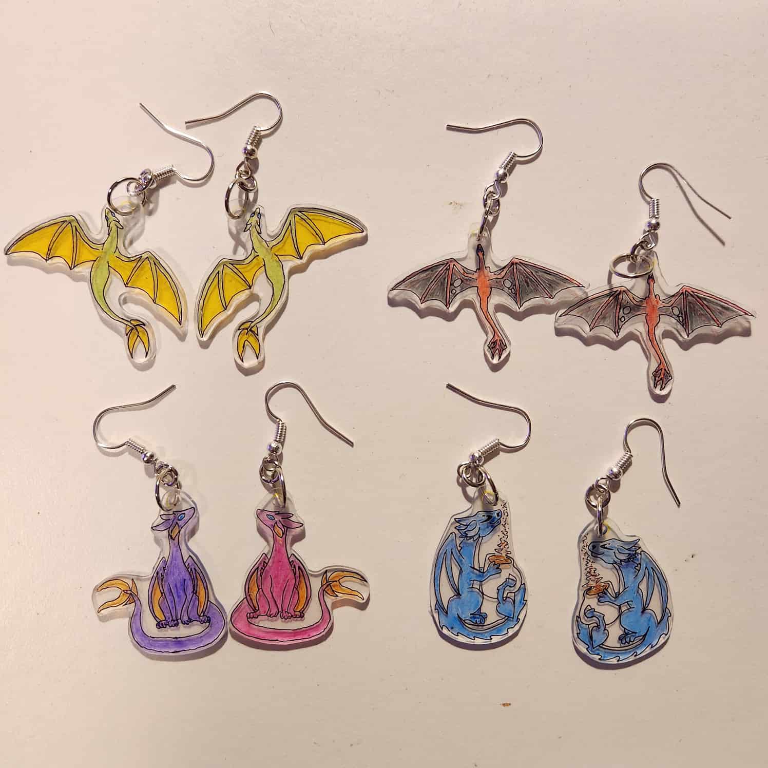 Four pairs of earrings made of shrink plastic. The plastic is clear, and they are all designs of dragons.