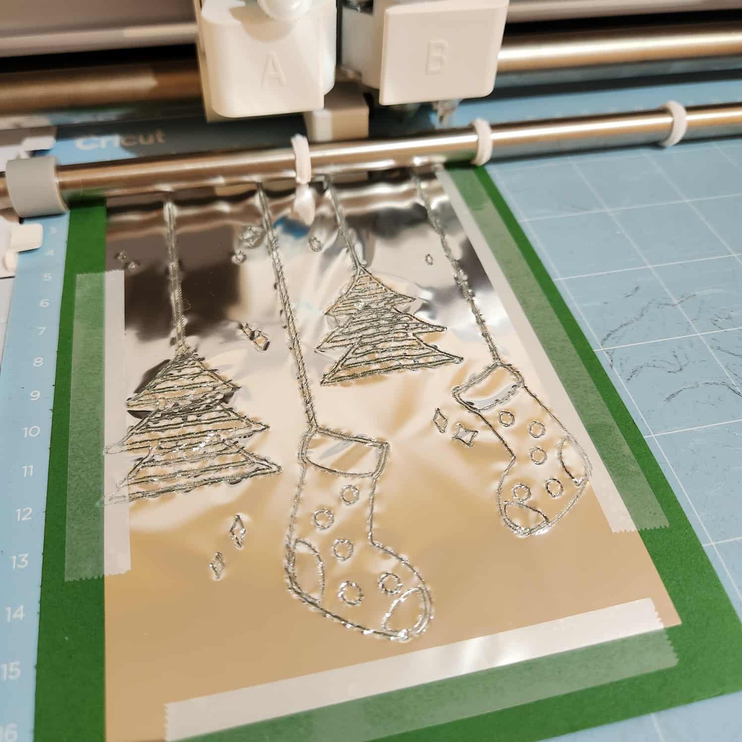 The green card with the foil taped to it, mounted on a Cricut mat and loaded into the front of a Cricut machine.