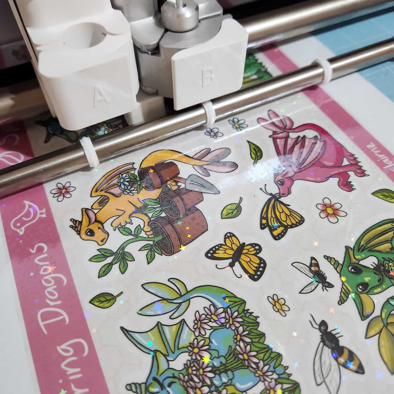 A dragon-themed sticker sheet loaded onto a cutting mat and into the front of a Cricut machine. It has not yet been cut.