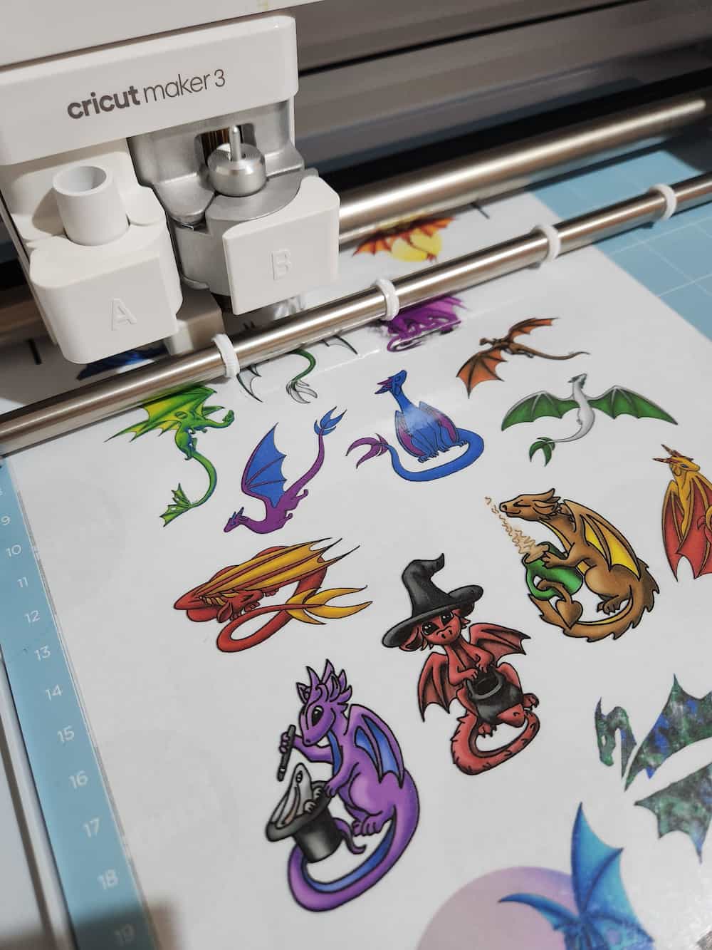 A dragon-themed sticker sheet loaded onto a cutting mat and into the front of a Cricut machine. It has not yet been cut.