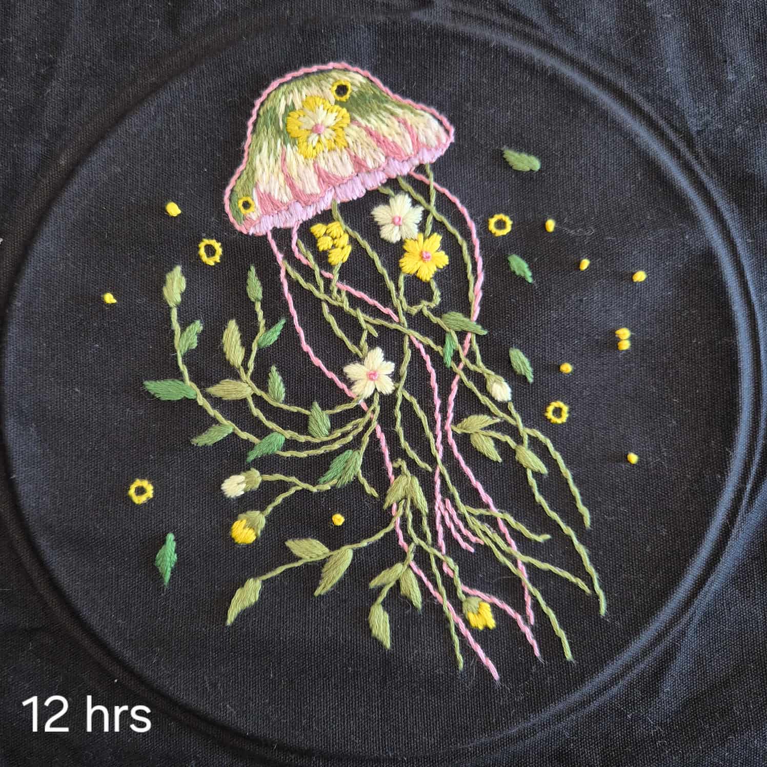 A green, yellow and pink embroidered jellyfish on a black cloth. The tentacles include flowers and vines. Text in the bottom left states 12 hours.
