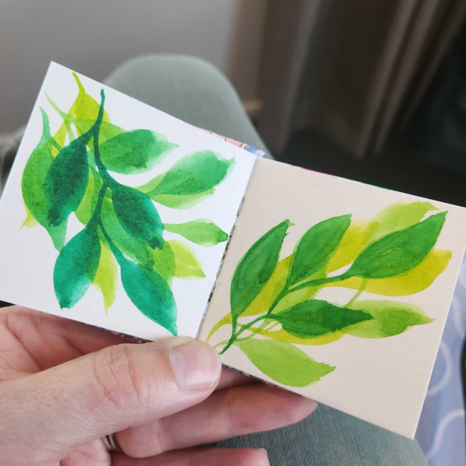 A small watercolour book open to two pages, both showing simple layered green leaf designs.