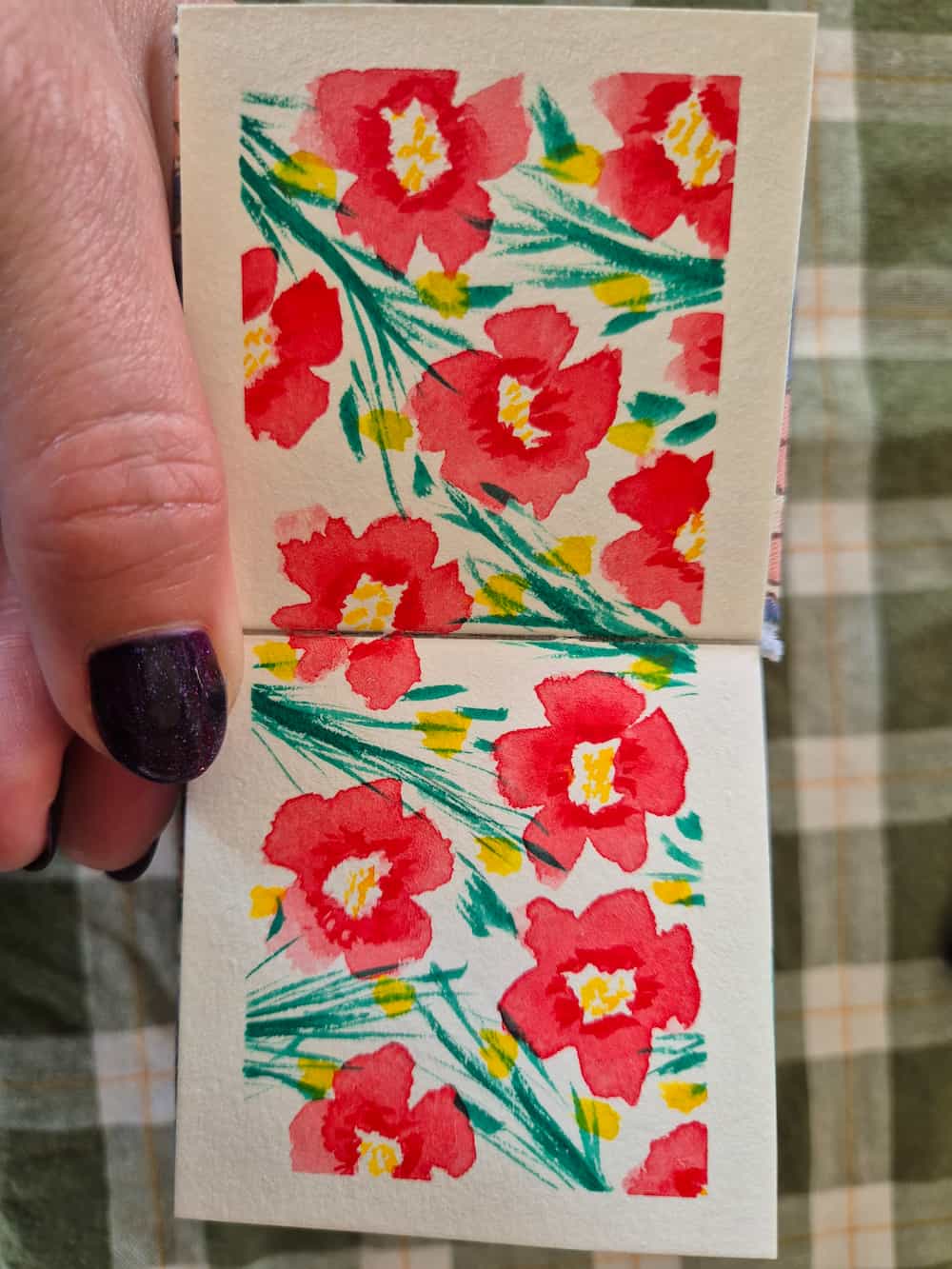 A small watercolour book open to a two-page spread of poppies and grass.