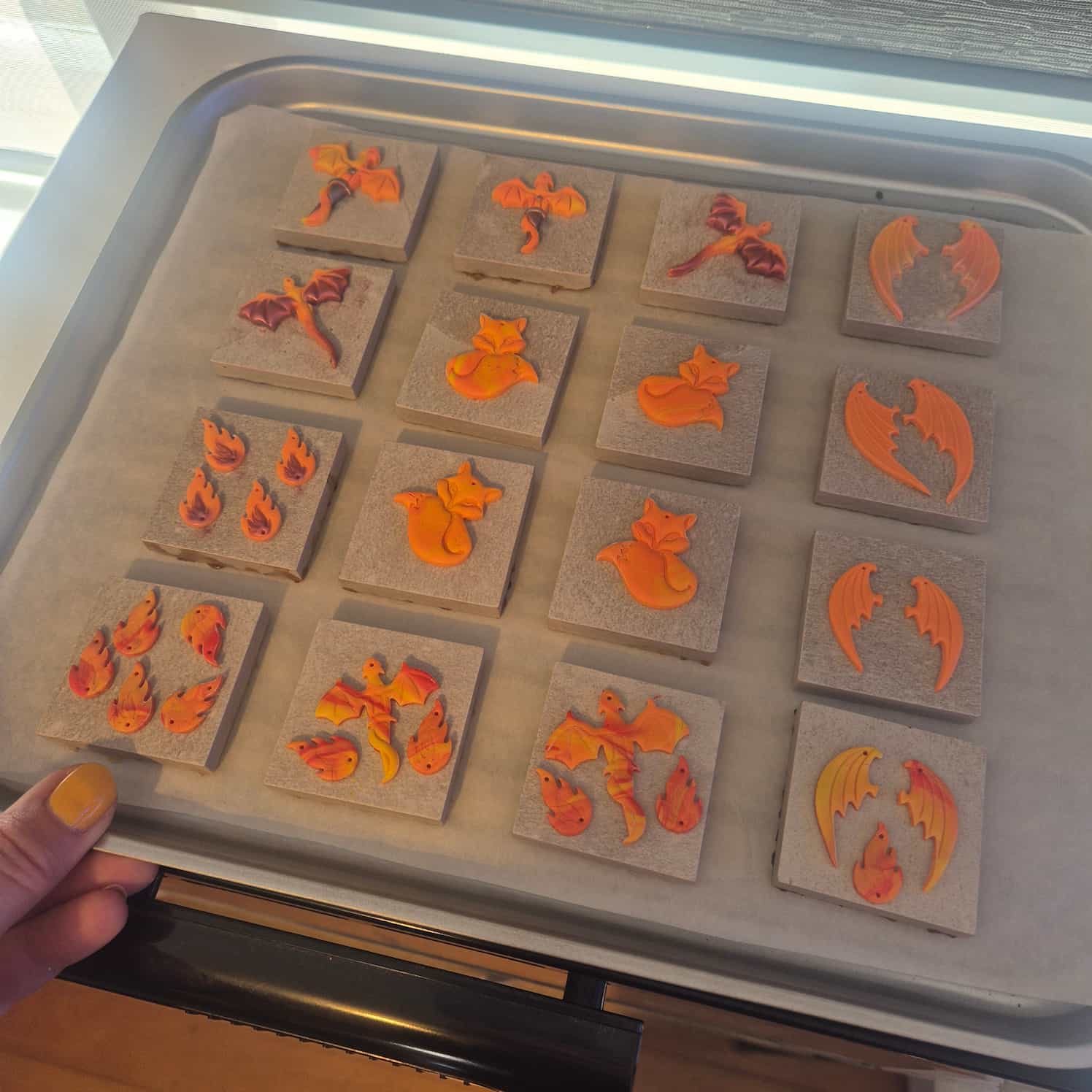 A wide shot of the orange and yellow polymer clay flat cut designs mounted on small grey tiles and placed on a baking tray, ready to go in the oven.
