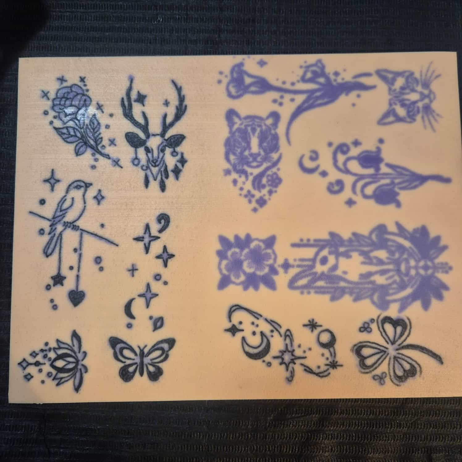 A practice tattoo skin showing many different small designs - flowers, birds, deer, butterflies. Some designs are not yet finished.