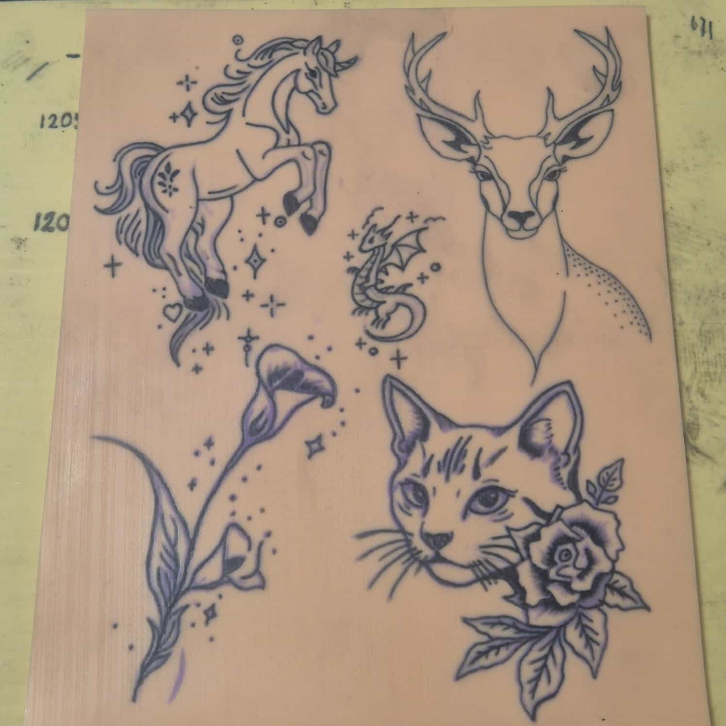 A practice tattoo skin showing five designs - unicorn, dragon, deer, lily, and cat.
