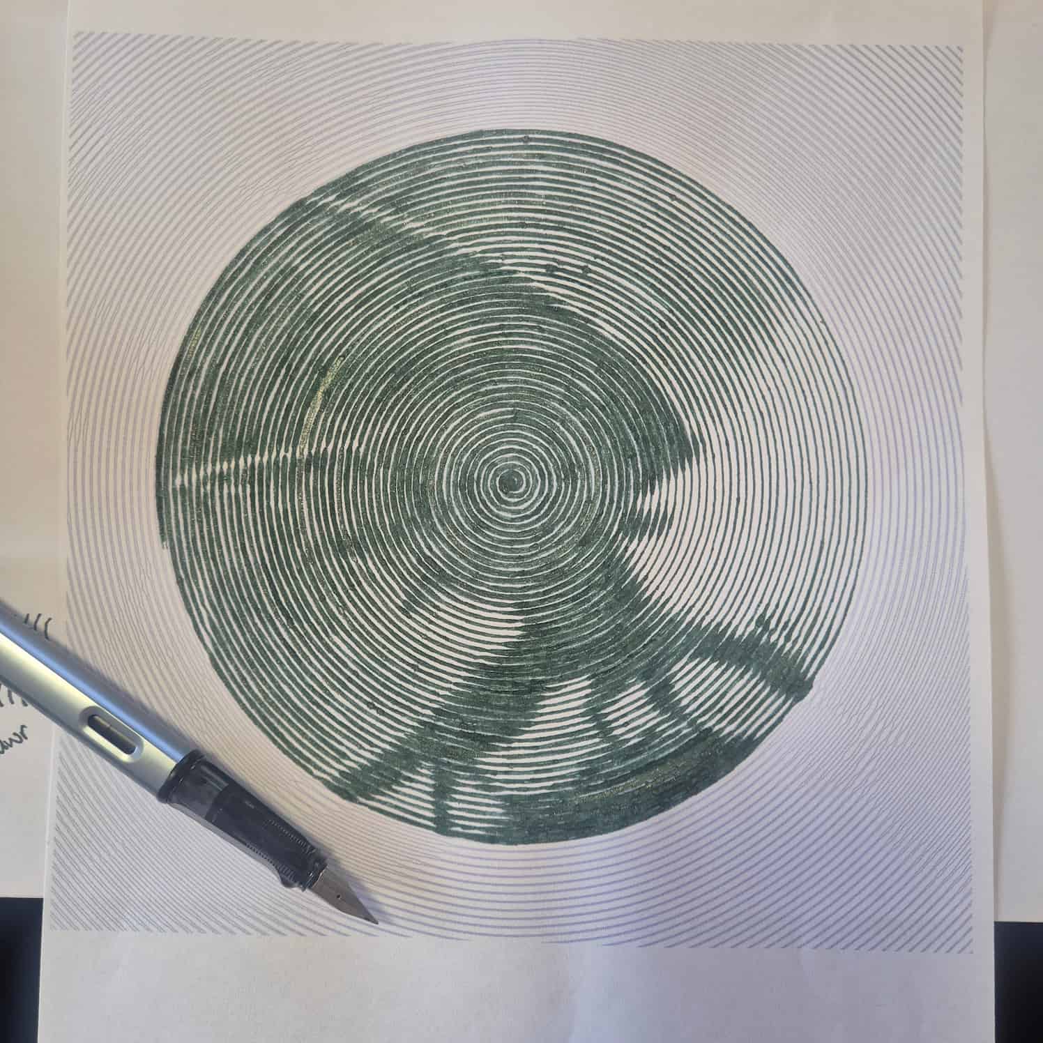 Coloured spiral art of a dragon in profile, with wings spread up. The design is not yet complete. A fountain pen is lying on the paper.