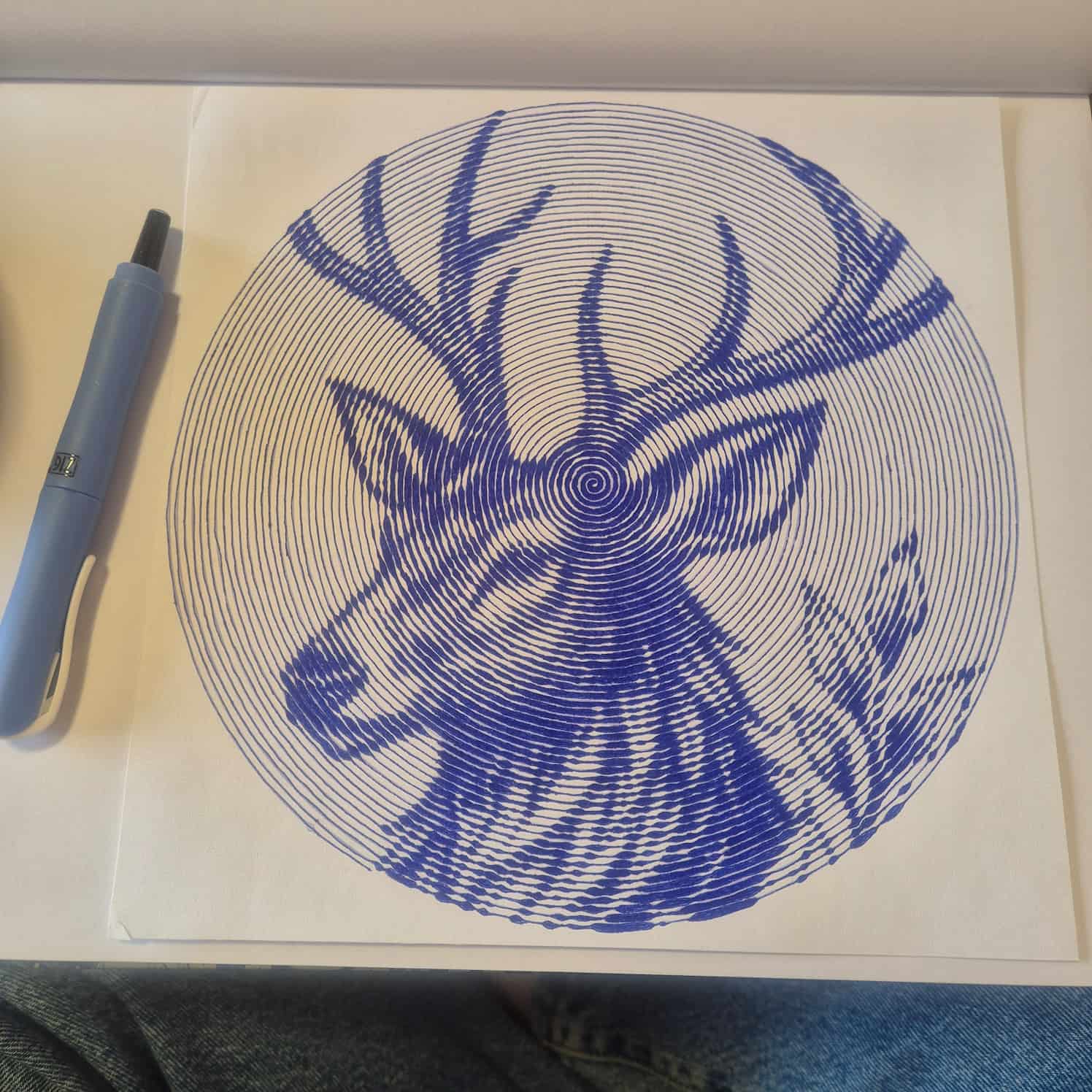 A completed spiral design of a deer head. A pen is lying on the paper.