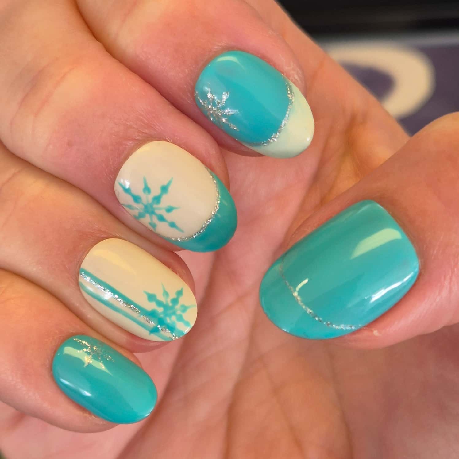 Light blue and cream snowflake nail design with glittery silver highlights.