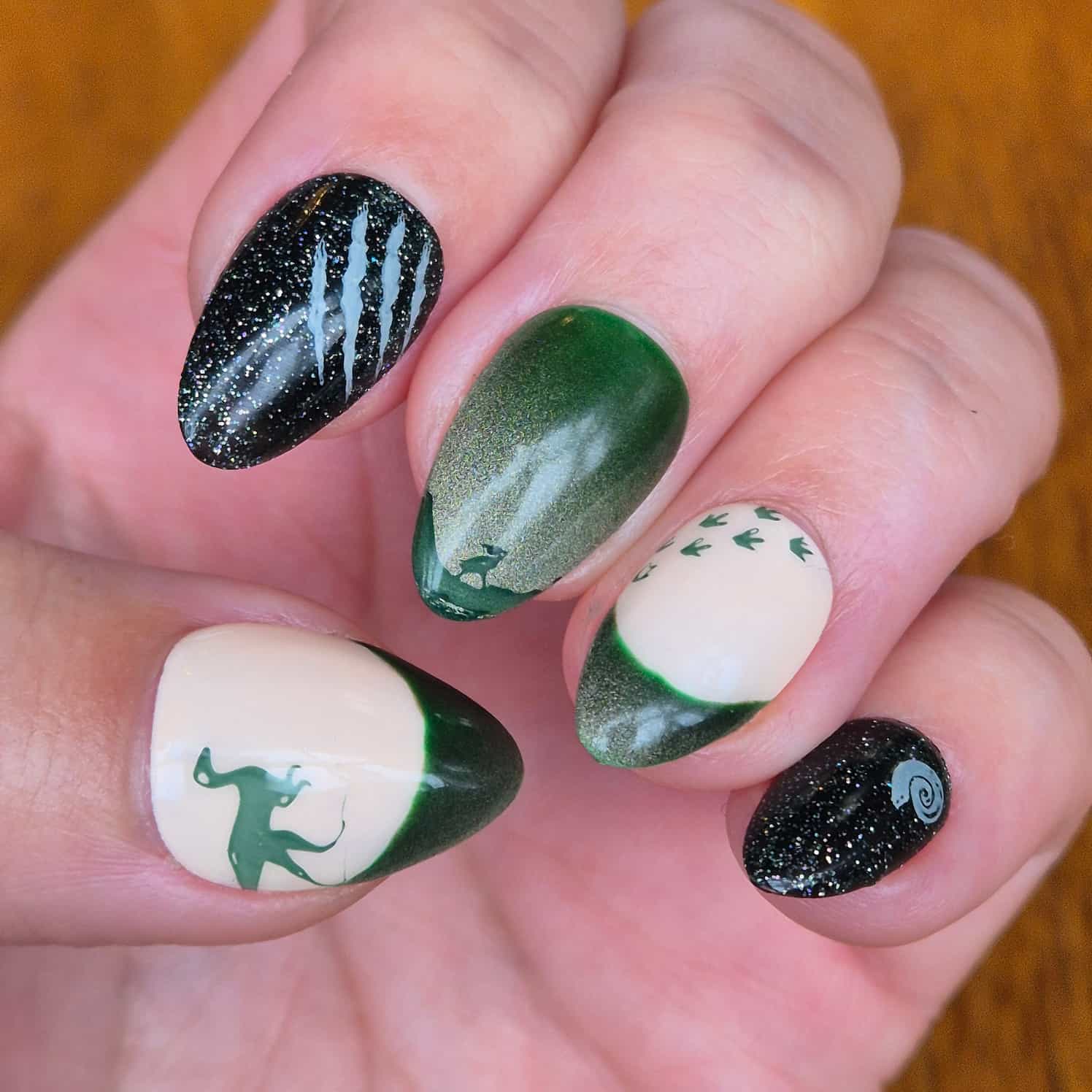 Green, cream and glittery black dinosaur-themed nail design.