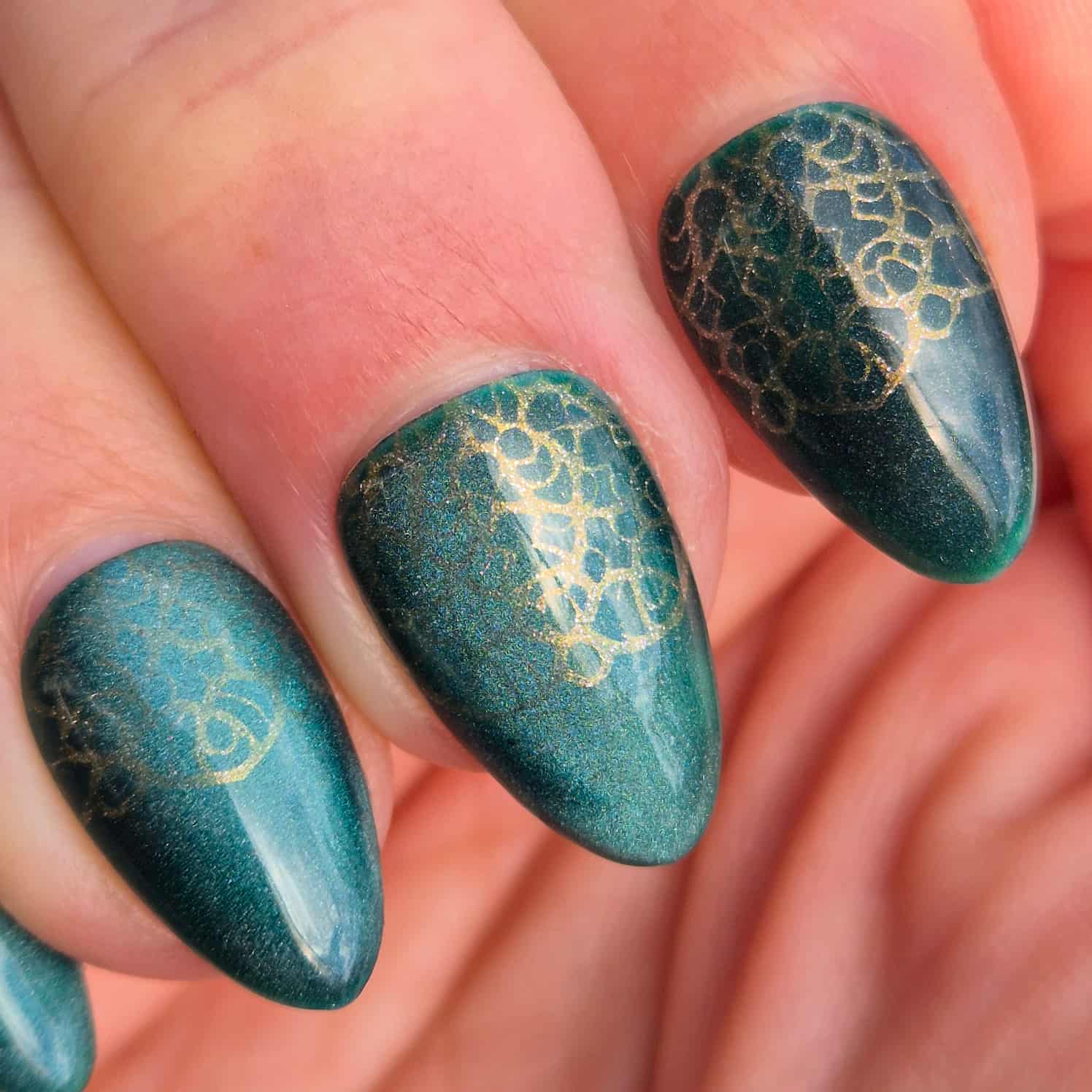 Extreme close-up of three nails showing a shimmery green nail with a subtle gold lace design stamped over half of each nail.