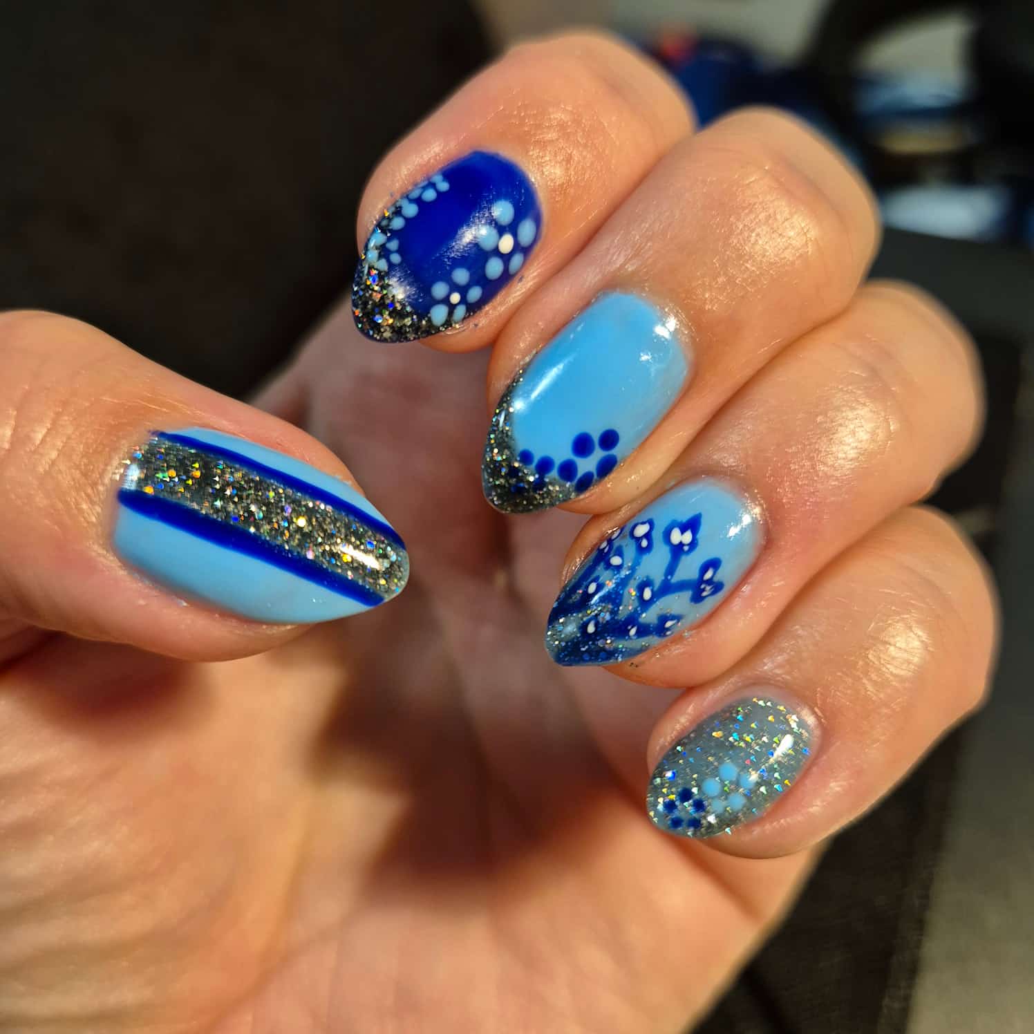 Abstract blue nail design with stripes and dots and silver glitter.