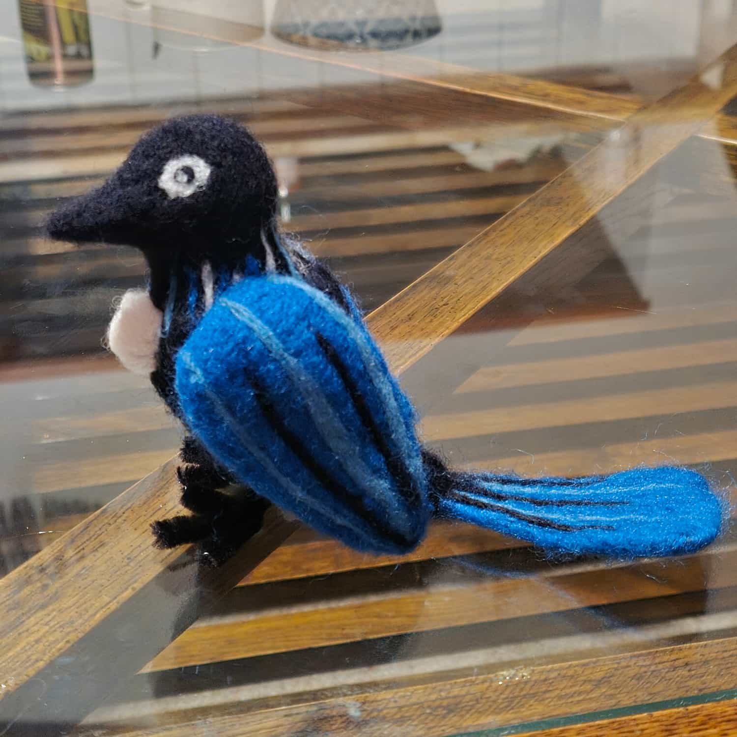 A needle felted tui bird in blue and black, seen from the other side. The distinctive white chest puff is more visible in this shot.