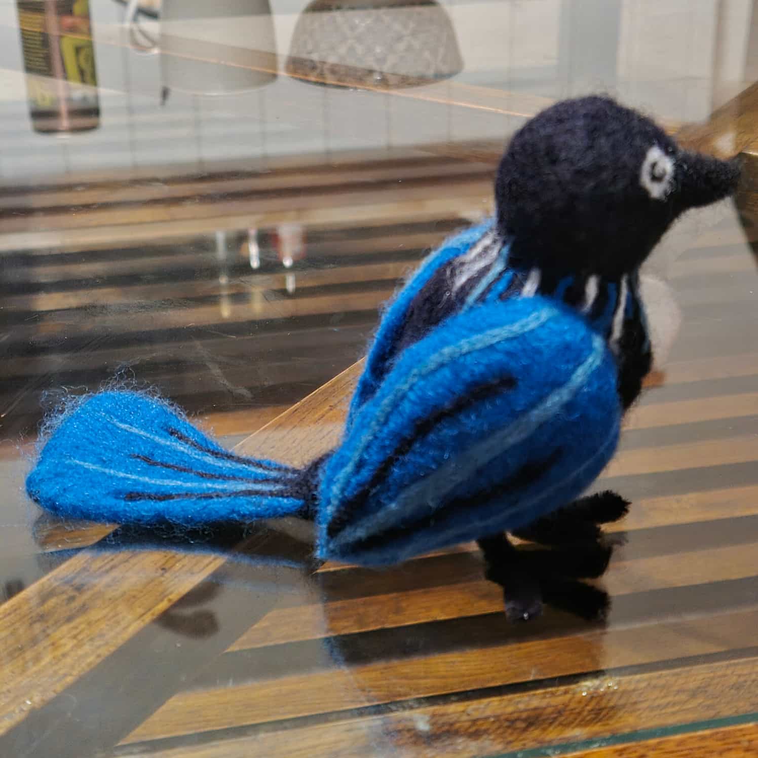 A needle felted tui bird in blue and black, seen from the side.