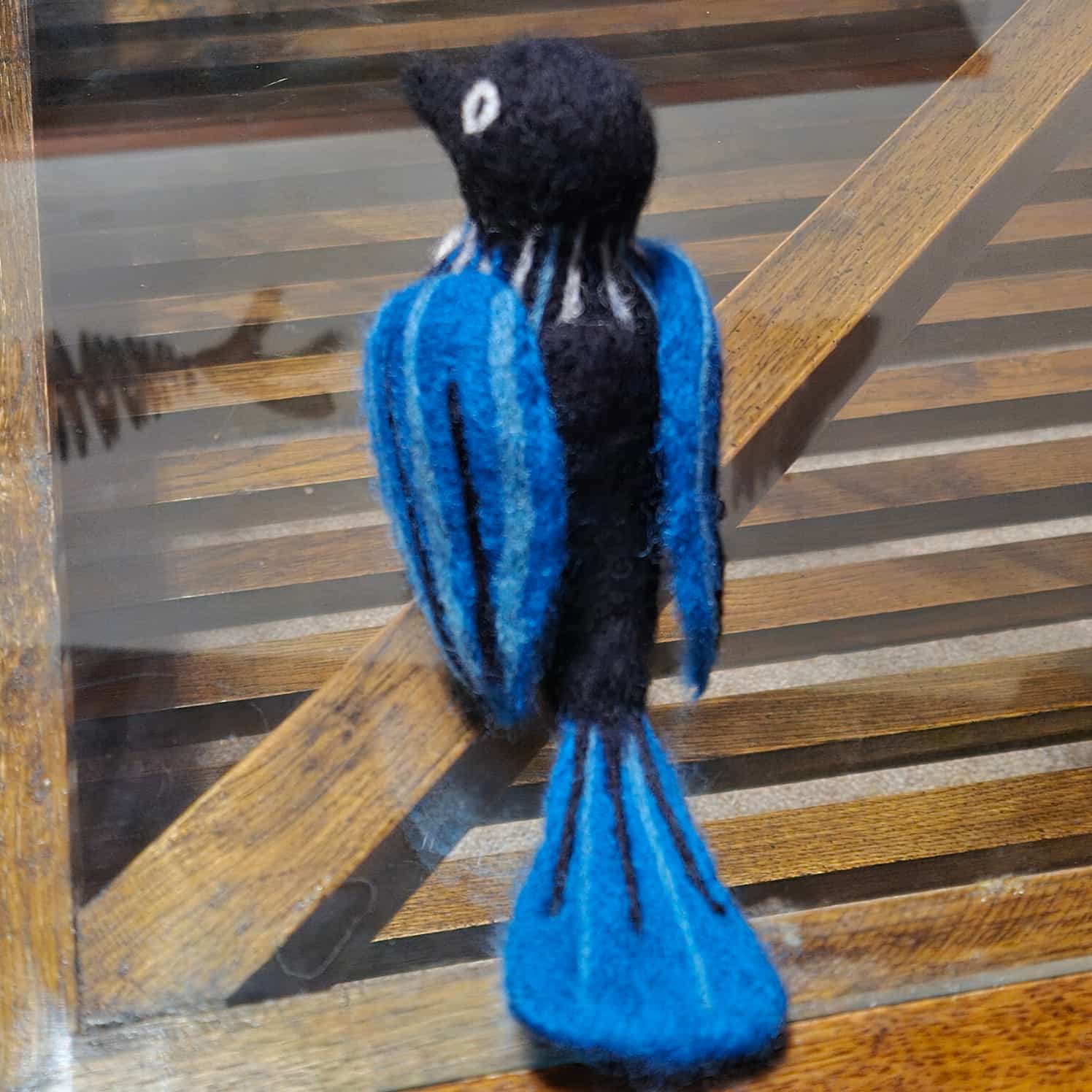 A needle felted tui bird in blue and black, shown from the back so you can see the wing and tail design better.