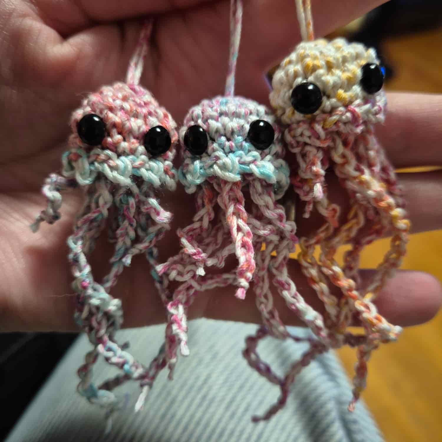 Three small crocheted jellyfish in pink, blue and yellow.