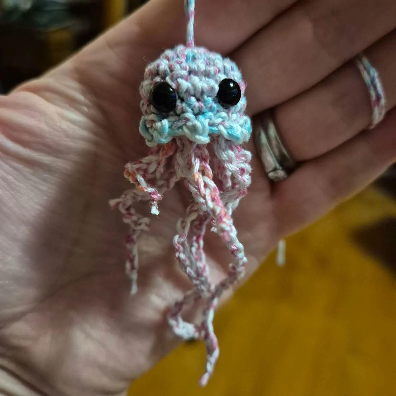 A small crocheted yellyfish. It has a red, blue and white head, red and white tentacles. It has black bead eyes.