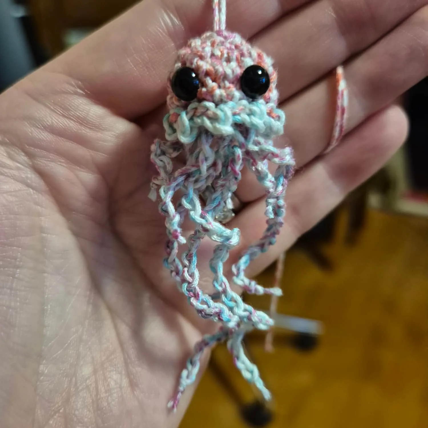 A small crocheted jellyfish. It has a red and white head, red and blue tentacles. It has black bead eyes.